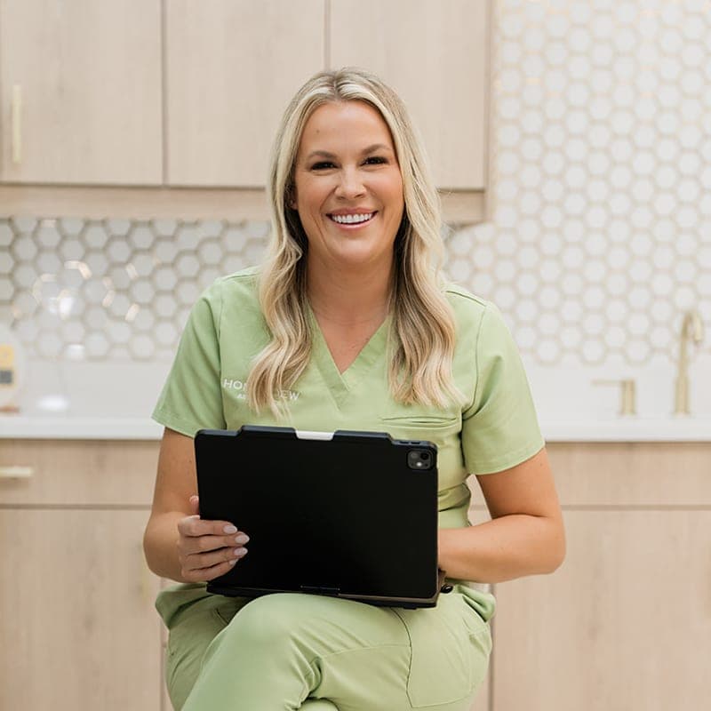 Taryn, RN, seated with a tablet in the Honeydew Aesthetics treatment room