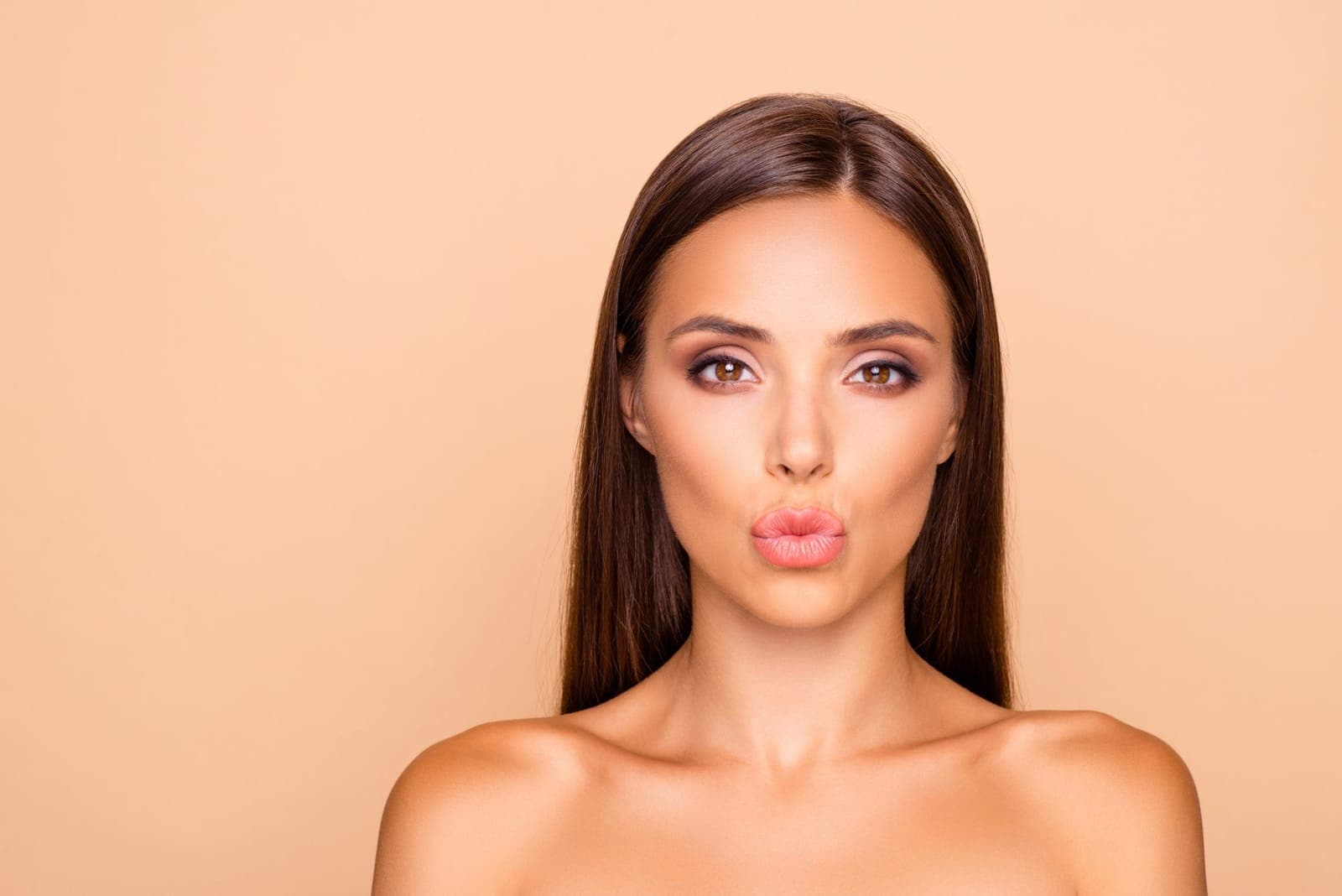 Woman with long brown hair pursing her lips against a peach background