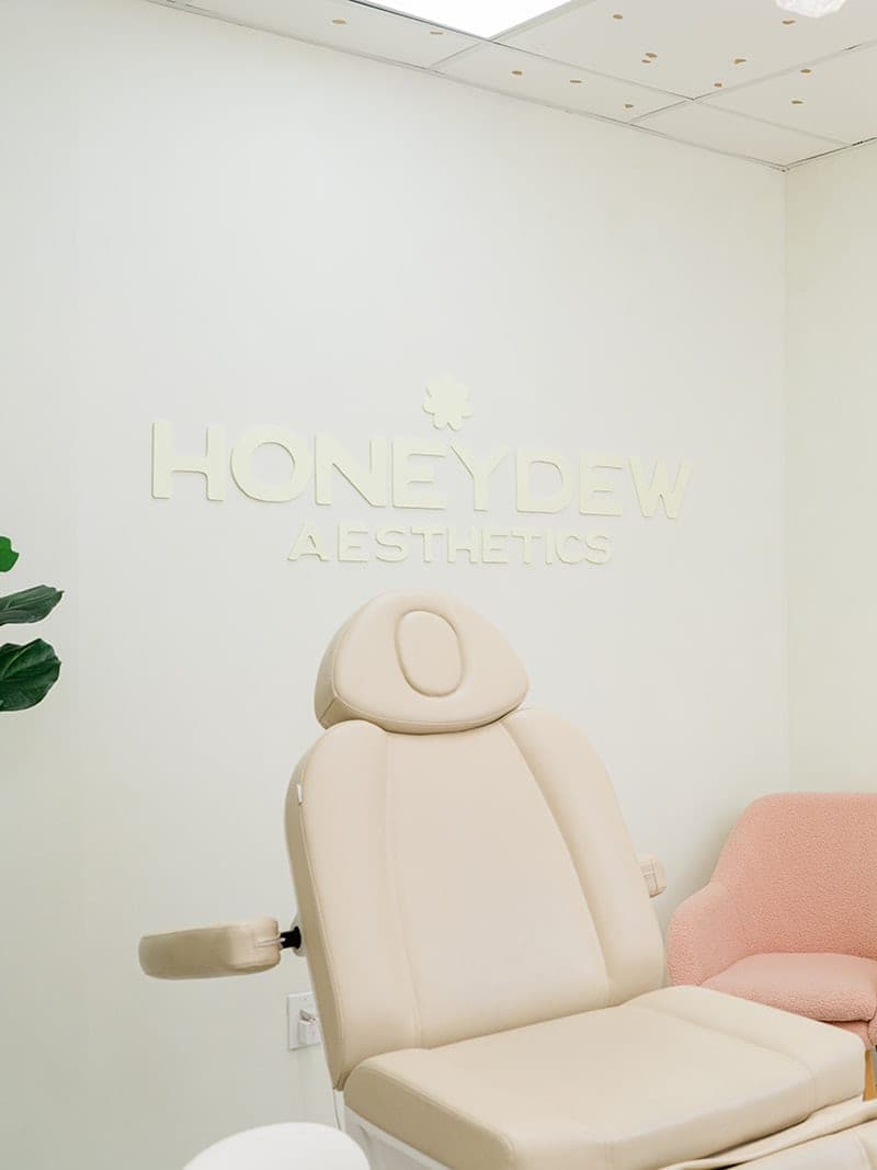 Honeydew Aesthetics treatment room with the wall logo, a treatment chair and a pink armchair