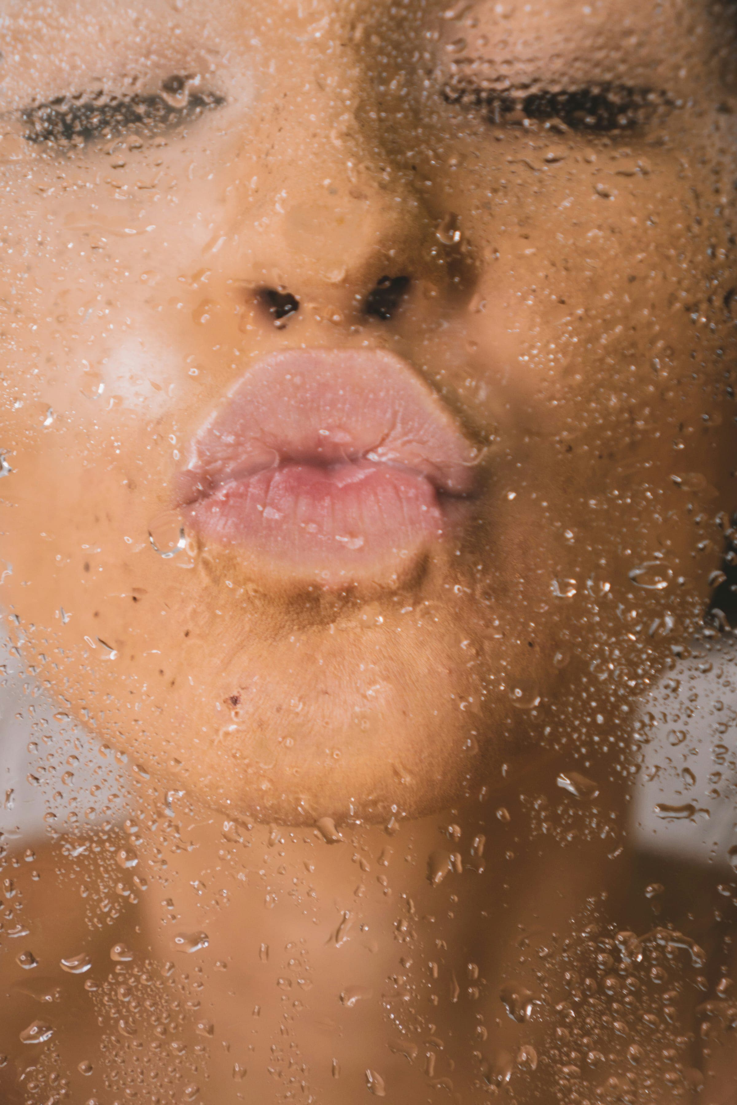 Close-up of pursed lips behind water-speckled glass